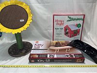 Full lot overview with all items: sunflower cat scratcher, boxed Merry and Bright holiday house, Kitty Sill cat perch box, and black dual bowl feeder.