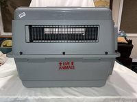 Front view of large plastic pet carrier crate with metal wire front door and ventilation slots. Shows 'LIVE ANIMALS' marking on the side.