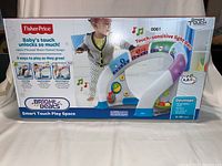 Front view of boxed Fisher-Price Bright Beats Smart Touch Play Space showing baby with product and features such as touch-sensitive light bar and kid playing with the toy.