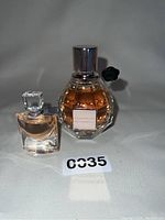 Close-up photo of two perfume bottles, one Flowerbomb by Viktor & Rolf and a smaller Lancôme bottle, showing details of bottles, caps, and liquid inside.