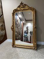 Full view of the gold gilt French Victorian style mirror leaning against wall in room.