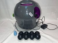 Front view of launcher with power cable, five black balls in front and two blue dog chew toys to the left