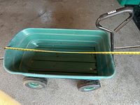 Top view showing the green plastic bed of the wagon with some surface rust and a measuring tape laid across the bed width.