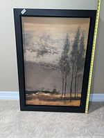 Full front view of the framed landscape painting showing the tree scene and neutral color palette with a measuring tape showing height.