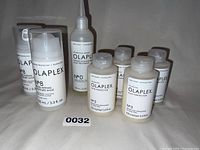 Photo showing 2 bottles of Olaplex No.8, 1 bottle of No.0, and 4 bottles of No.3 on a white cloth background.