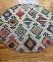 Top view showing round carpet with colorful geometric diamond patterns on wooden floor, tape measure across center indicating size.