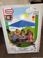 Front view of box showing product image of children seated at picnic table with blue umbrella.