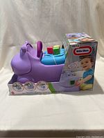 Purple hippo ride-on toy in original packaging with some colorful blocks on seat, placed against a neutral background showing left side view.