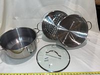 Full view of steamer set components arranged with glass lid front and center, featuring large pot, two perforated steamers, and glass lid.