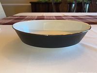 Oval-shaped serving bowl with black exterior and silver rim, showing side profile on table