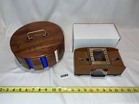 Photo showing the poker chip set in a round wooden case and the brown automatic card shuffler side by side with measuring tape for size reference.