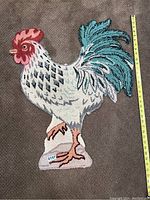 Photo showing the front of the rooster kitchen rug with measuring tape vertically along the right side to show height measurement around 20 inches.