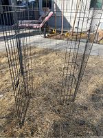 Black metal wire critter fence panels arranged outdoors on grass, showing tall rectangular panels and a hinged door with latch.