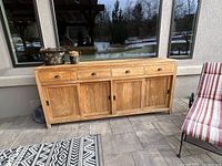 Full front view of teak credenza with all doors and drawers closed, showing wood grain, metal cup handles on drawers, and sliding doors.