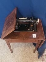 View of 1927 Singer sewing machine partially exposed under the cabinet lid, showing the machine mounted in the solid wood table.