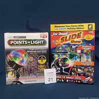 Boxed LED Points of Light projector and Star Shower Slide Show box with colorful holiday-themed projections illustrated