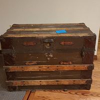 Front view of antique steamer trunk showing wood strips, leather trim, and front lock.