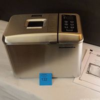 Breadman Pro TR900S bread machine front view showing control panel and top lid with viewing window. Instruction manual visible on the right side.