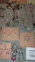 Various costume jewelry pieces including necklaces with pendants, dangling earrings, and Tinkerbell enameled sets arranged on display board.