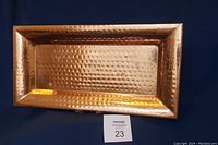 Full view of the rectangular hammered copper tray showing its textured surface and raised edges on a dark blue background.