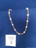 Full view of the necklace against blue background with freshwater pearls evenly spaced on a metal beaded chain.