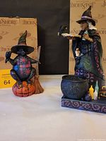 Both Halloween figurines with original Jim Shore boxes in the background. Witch with cauldron and black cat on pumpkin shown side by side.