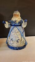 Front view of the 10-inch Jim Shore Blue Santa figurine showing detailed blue and white robe with winter village scene and Santa holding a string of blue lights.