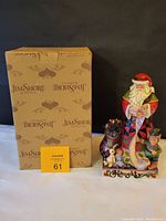 Photo of the Jim Shore box beside the two-sided Santa figurine with the auction tag in front