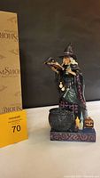 Front-side view of Jim Shore Halloween "Conjuring Up A Spell" witch figurine next to original box and auction lot number.