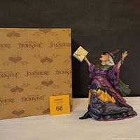 Front view of Jim Shore witch figurine standing next to original Jim Shore branded box
