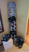 Full view of the Bud Light snowboard with bindings, men's snowboard boots, and Giro helmet grouped together showing overall condition and set.