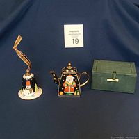 Full view of the three items: teapot, bell with ribbon, and box all displayed on a blue cloth.