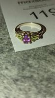 Front angled view of silver ring showing the 6 mm round amethyst center stone and 5 mm pear-shaped peridot stones on each side.