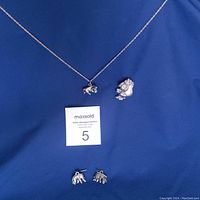 Pewter Eeyore jewelry set displayed on blue fabric including necklace with chain and pendant, brooch, and small stud earrings.