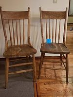 Two vintage wooden chairs with spindled legs and carved floral pressed backs in natural wood finish