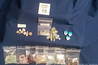 Photo of three glass heart pendants and nine bags of beads arranged on blue fabric. Pendants are heart shaped with blue and white glass. Bags contain various quartz, fluorite, agate, and glass beads in multiple colors and sizes.