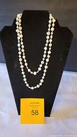 Front view of seed pearl necklace draped twice on a black necklace display stand showing length and pearl detail.