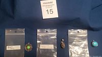 All three pendants displayed in labeled baggies on blue fabric background with auction tag