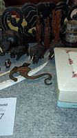 Photo showing vintage elephant figurines including metal mother/baby pair with damage, hand carved ebony figures, three human carvings, and ceramic/metal decorative items on a gray surface.