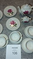 Porcelain vintage children's tea set displayed with plates, saucers, cups, teapot, sugar bowl and creamer, all decorated with pink rose motif.