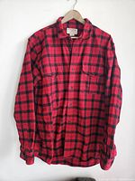 Front view of the Filson Alaskan Guide shirt hanging on a hanger, showing red and black plaid pattern and two chest pockets.