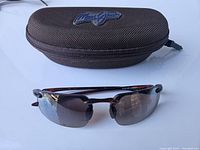 Photo of the brown zippered Maui Jim carrying case and rimless sunglasses on a white surface.