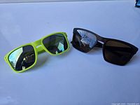 Two pairs of Oakley sunglasses: brown with prescription lenses and neon yellow with regular marked lenses.
