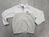 Full view of white and beige Patagonia fleece pullover laid flat showing front, collar, chest pocket, and sleeves.