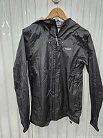 Front view of black Patagonia rain jacket with hood, showing full zipper and overall condition.