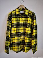 Front view of yellow and black plaid flannel shirt on hanger, showing button-up front and collar.