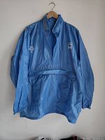 Front view of vintage light blue windbreaker with zippered collar and elastic cuffs hanging on hanger.