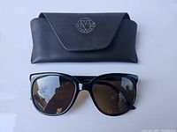 Front view of black Vuarnet vintage sunglasses with brown lenses alongside the black case showing embossed logo.