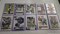 Top view of 10 Tom Brady football cards arranged in two rows in protective sleeves showing different card designs and images of Tom Brady in various poses.