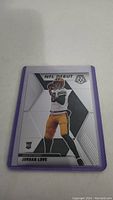 Photo of Jordan Love NFL Debut rookie card in purple protective sleeve, showing front side of card with player image and text